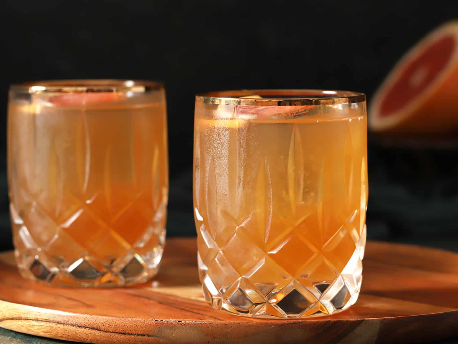 A pair of rocks glasses filled with Brown Sugar Grapefruit cocktail garnished with slices of fresh grapefruit.