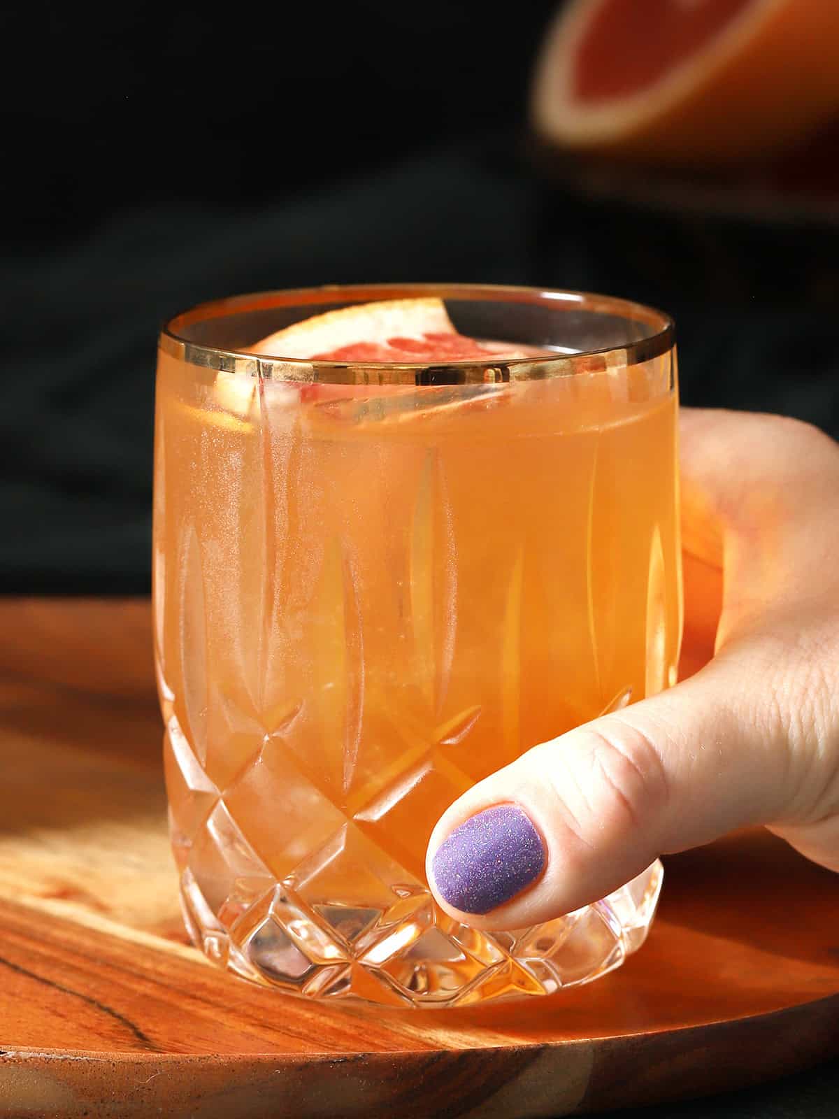 A hand picking up a glass of bourbon grapefruit cocktail. 