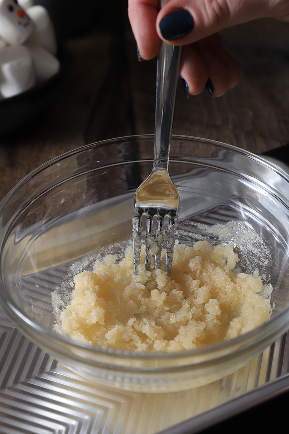 A hand using a fork to stir together white sugar and vanilla.