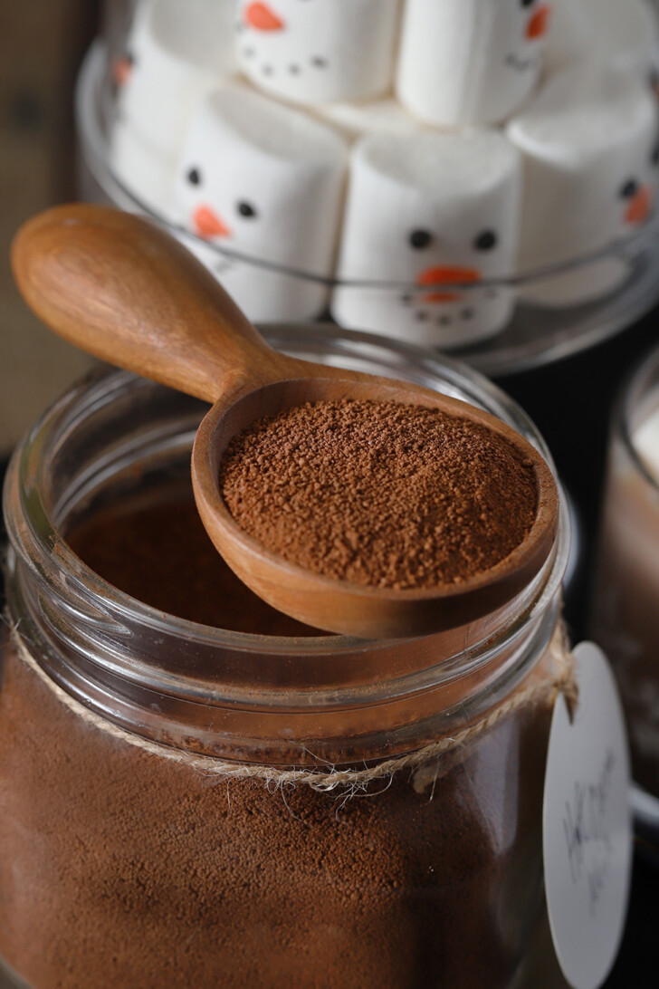 Hot cocoa mix in a wooden spoon on top of a jar filled with mix.