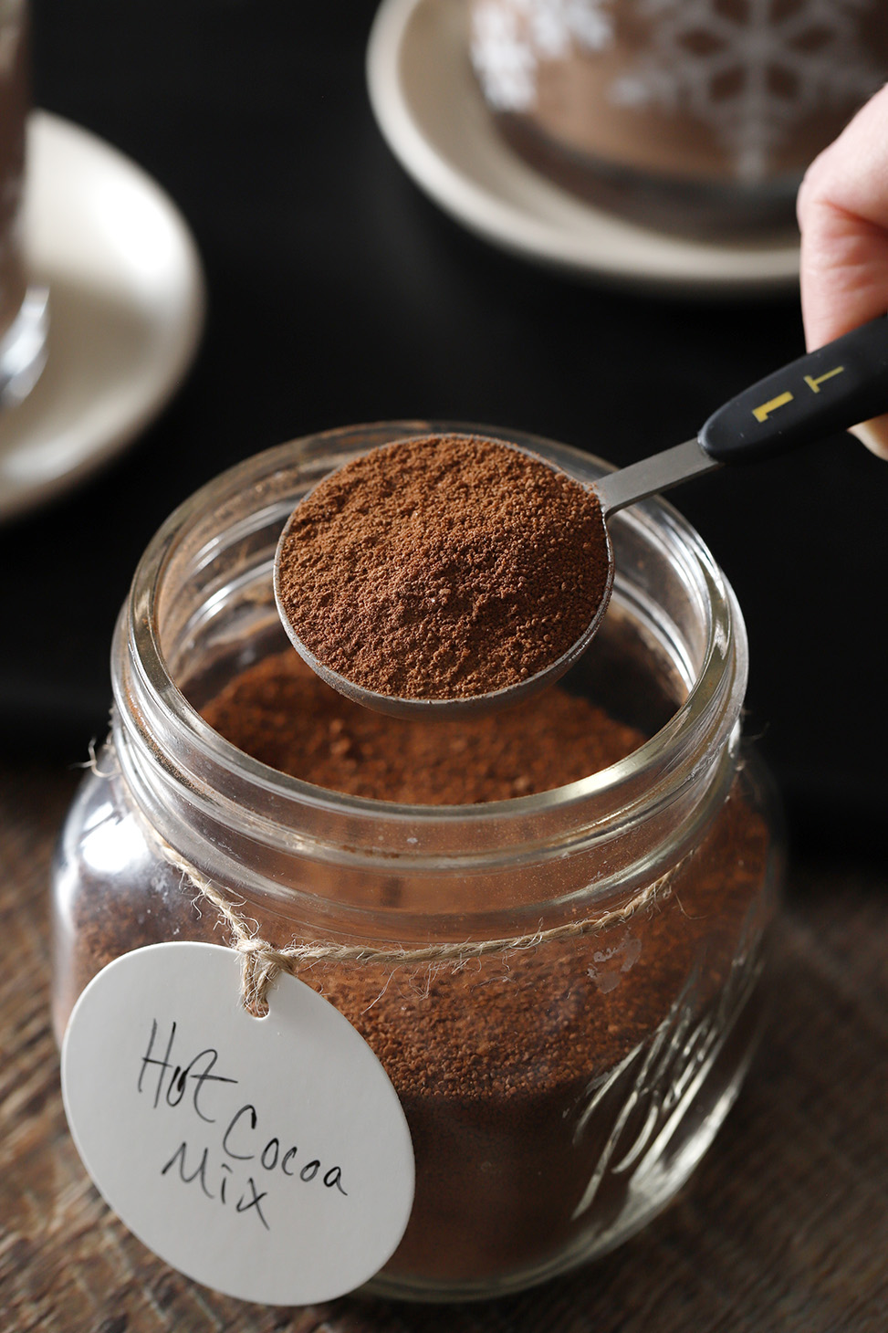 A hand measuring out a tablespoon of cocoa mix.