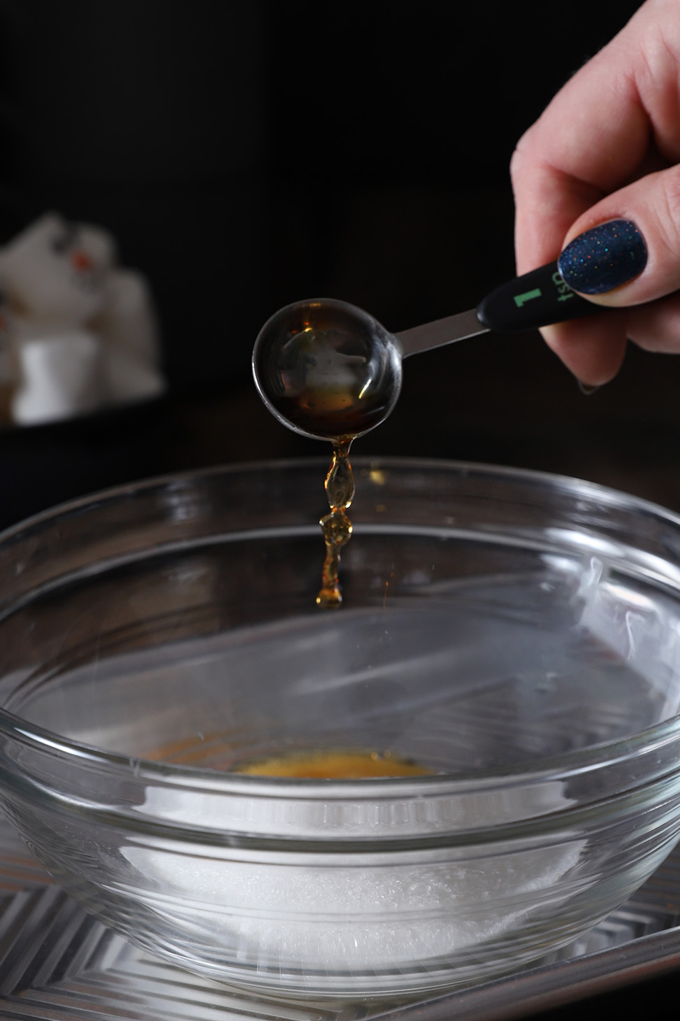 A hand pouring vanilla extract into a bowl of sugar.