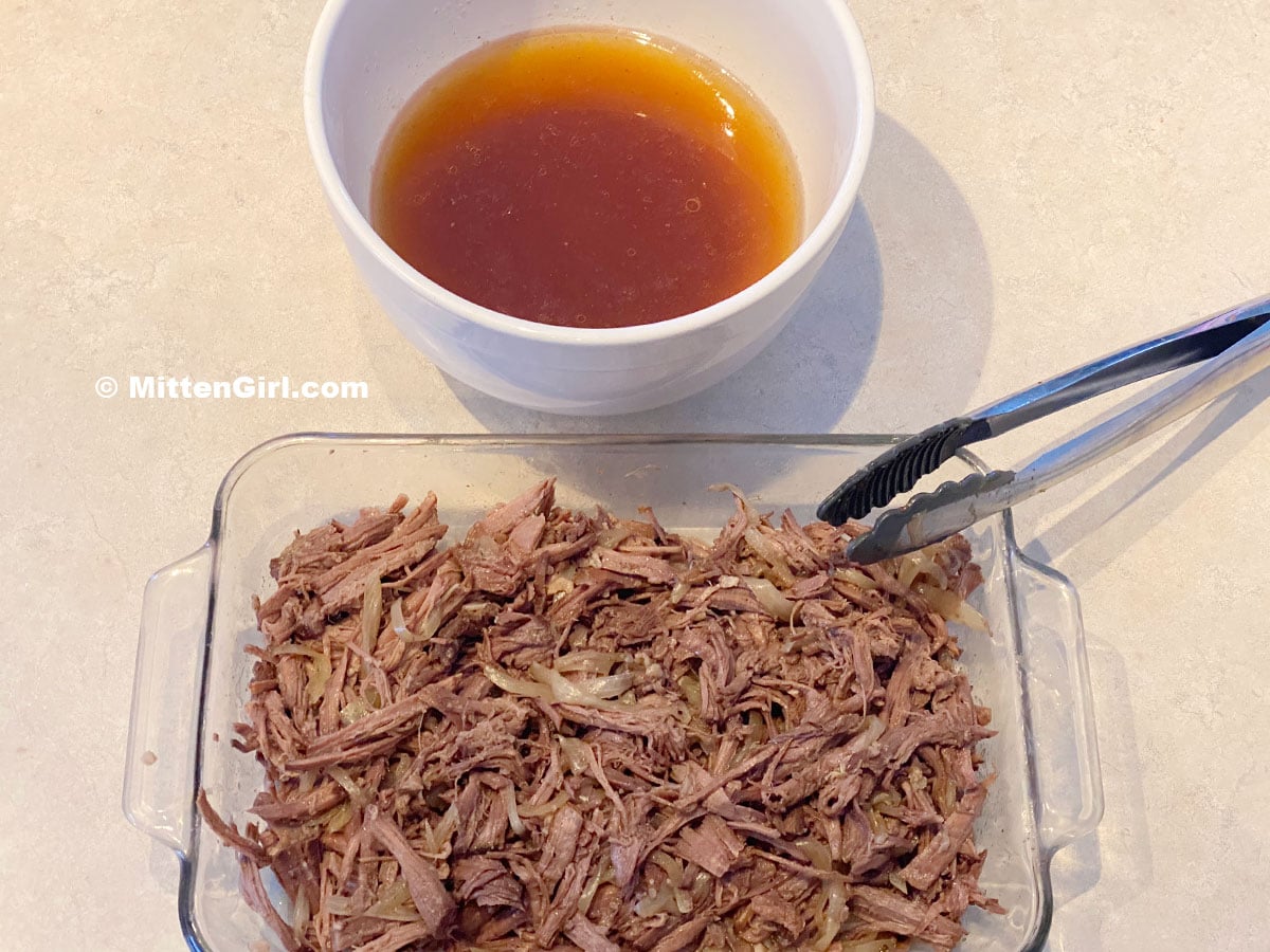Shredded beef and onion in a pan with a bowl of stock.