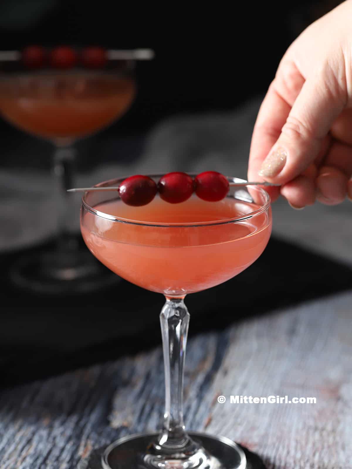 A hand garnishing a cocktail with cranberries.