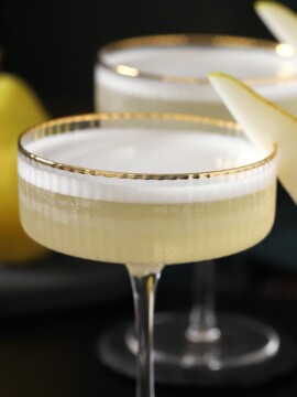 Couple glasses filled with pear vodka sour cocktails, garnished with slices of fresh pears.