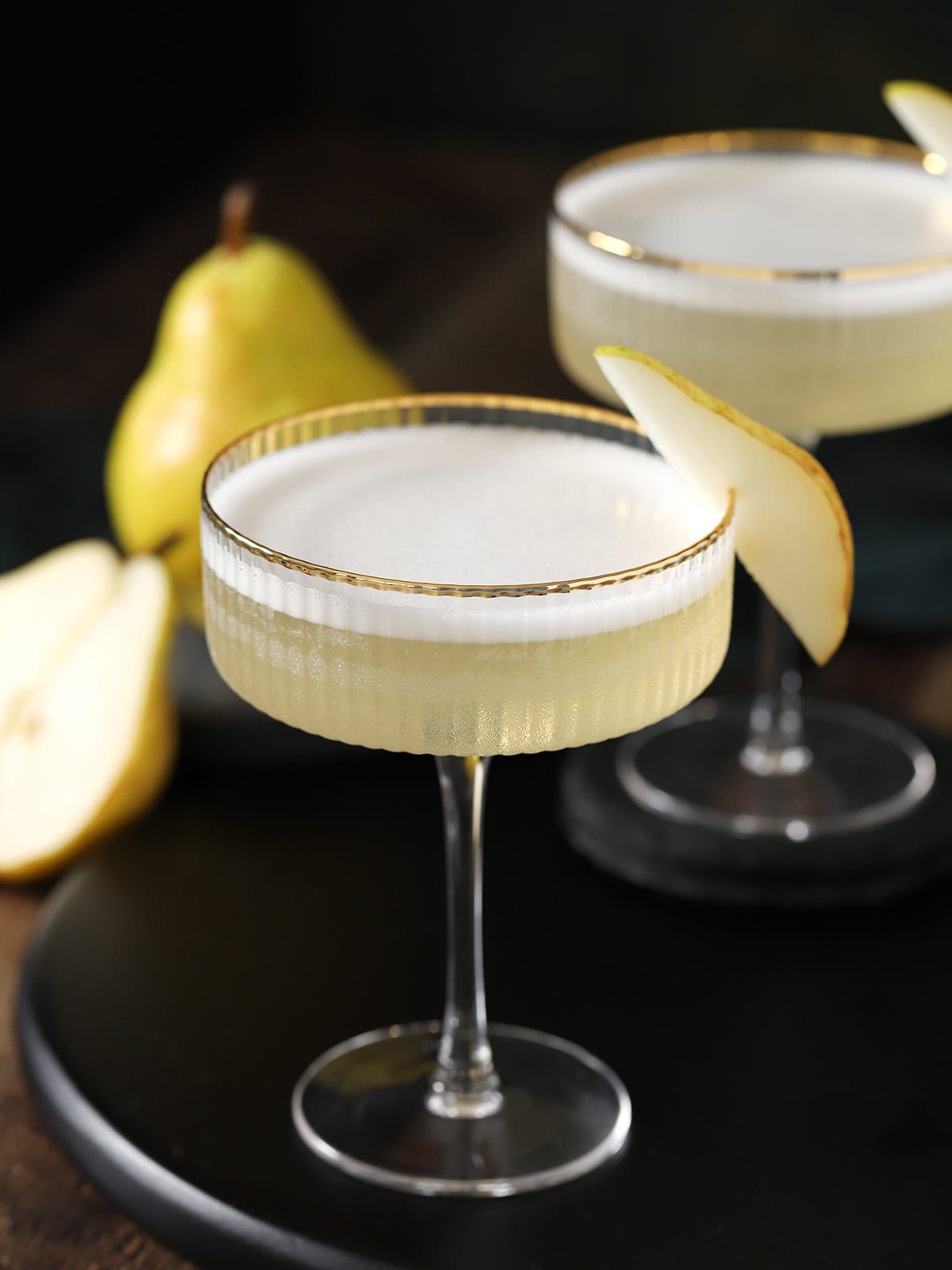 Couple glasses filled with pear vodka sour cocktails, garnished with slices of fresh pears.