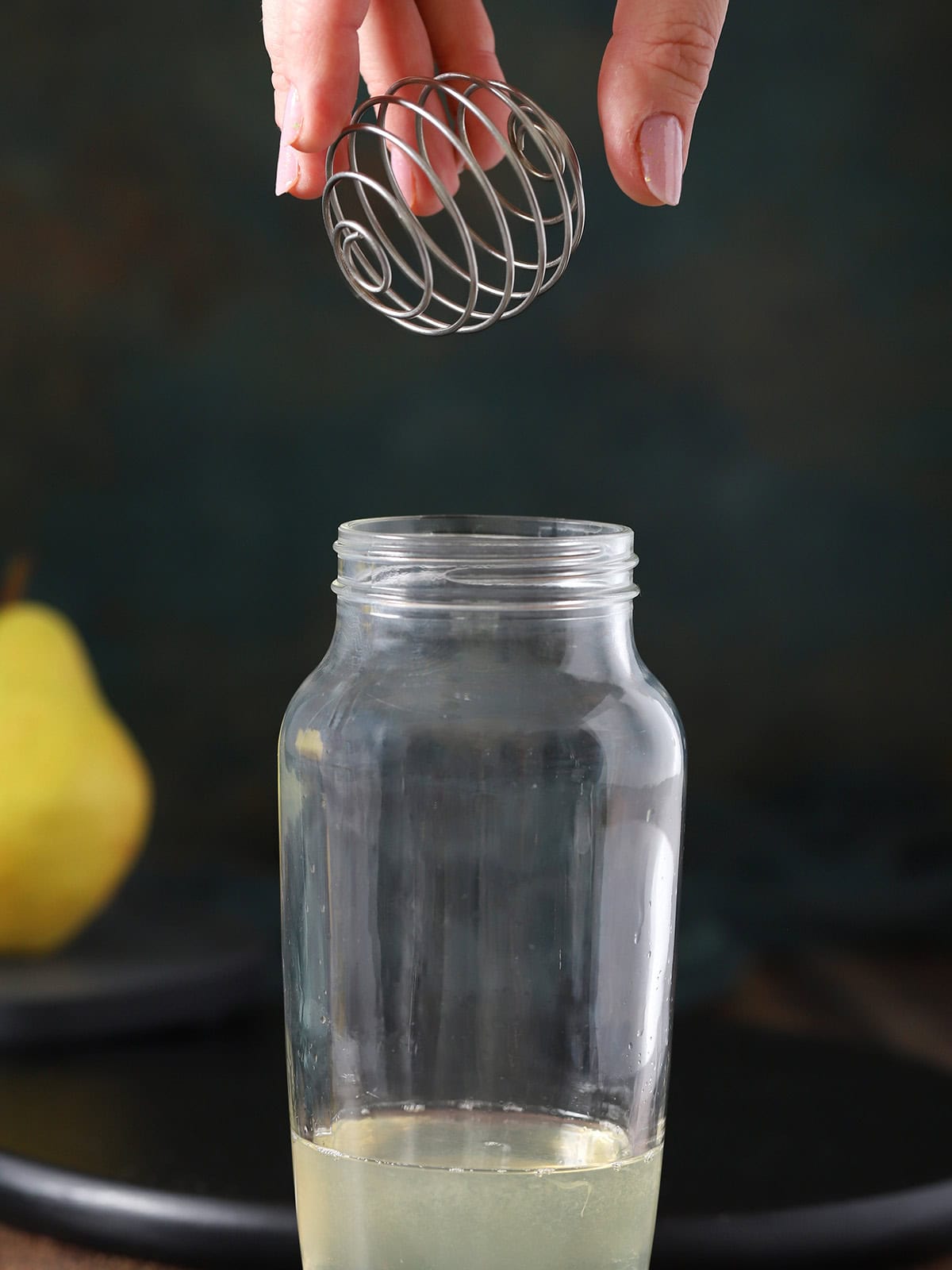 A hand dropping a ball whisk into a cocktail shaker.
