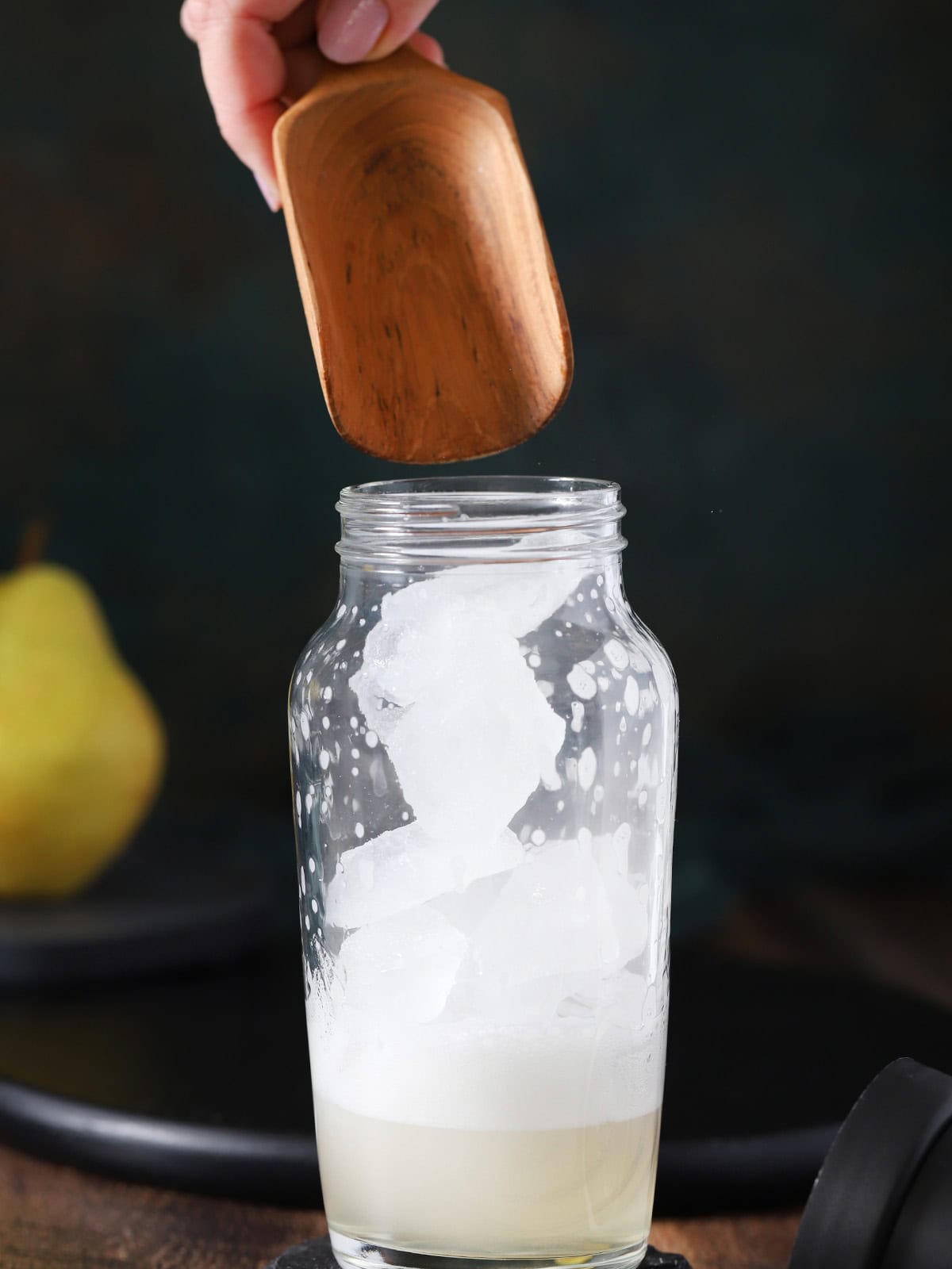Ice being poured from a wooden scoop into a cocktail shaker.