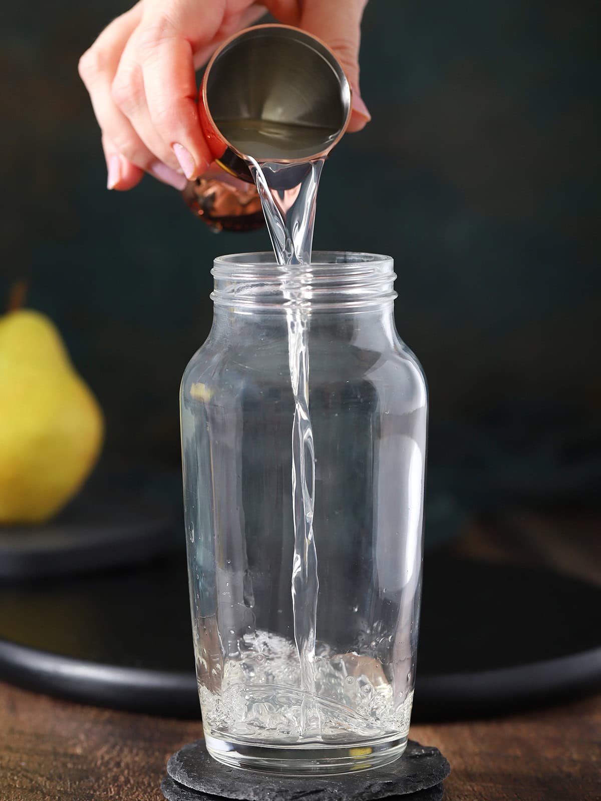 A hand pouring pear vodka into a cocktail shaker.