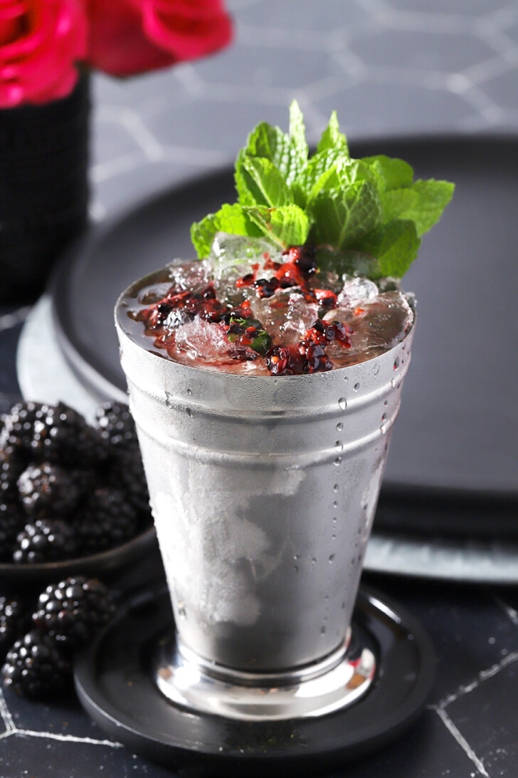 A blackberry mint julep in a silver julep cup with a large bunch of mint for garnish.