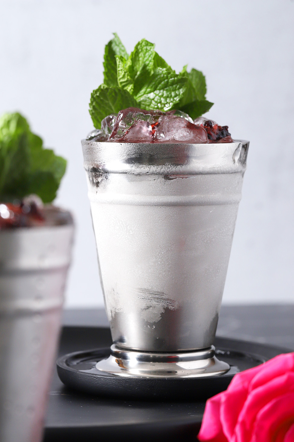 A blackberry mint julep in a silver julep cup with a large bunch of mint for garnish.