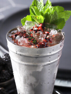 A blackberry mint julep in a silver julep cup with a large bunch of mint for garnish.
