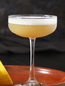 A glass of ginger bourbon sour cocktail on wooden trays with lemons.