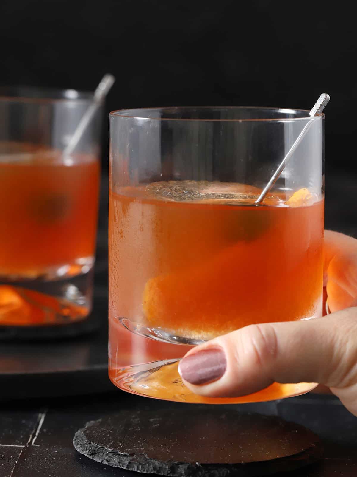 A hand picking up a rocks glass filled with old fashioned cocktail.