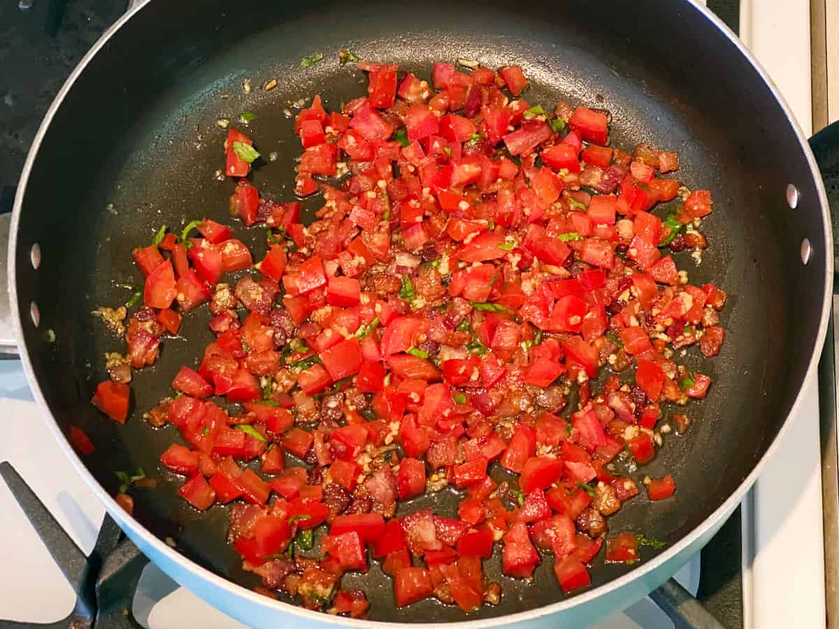 Diced tomatoes mixed with bacon, garlic, and lime juice in a pan