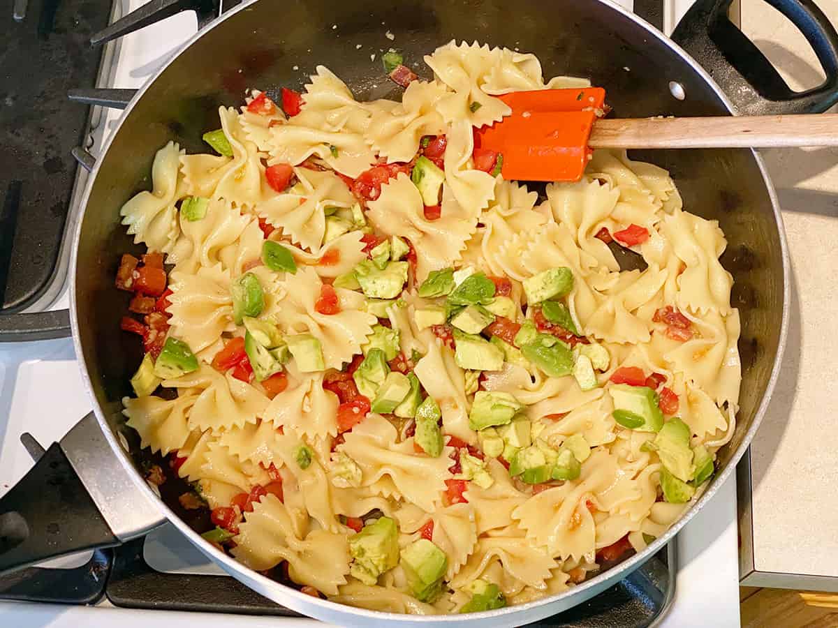 Avocado added to a skillet of pasta, bacon, tomatoes, garlic and lime juice.