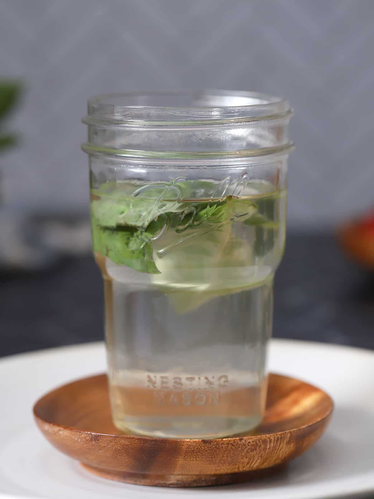 A jar of basil simple syrup on a small plate.