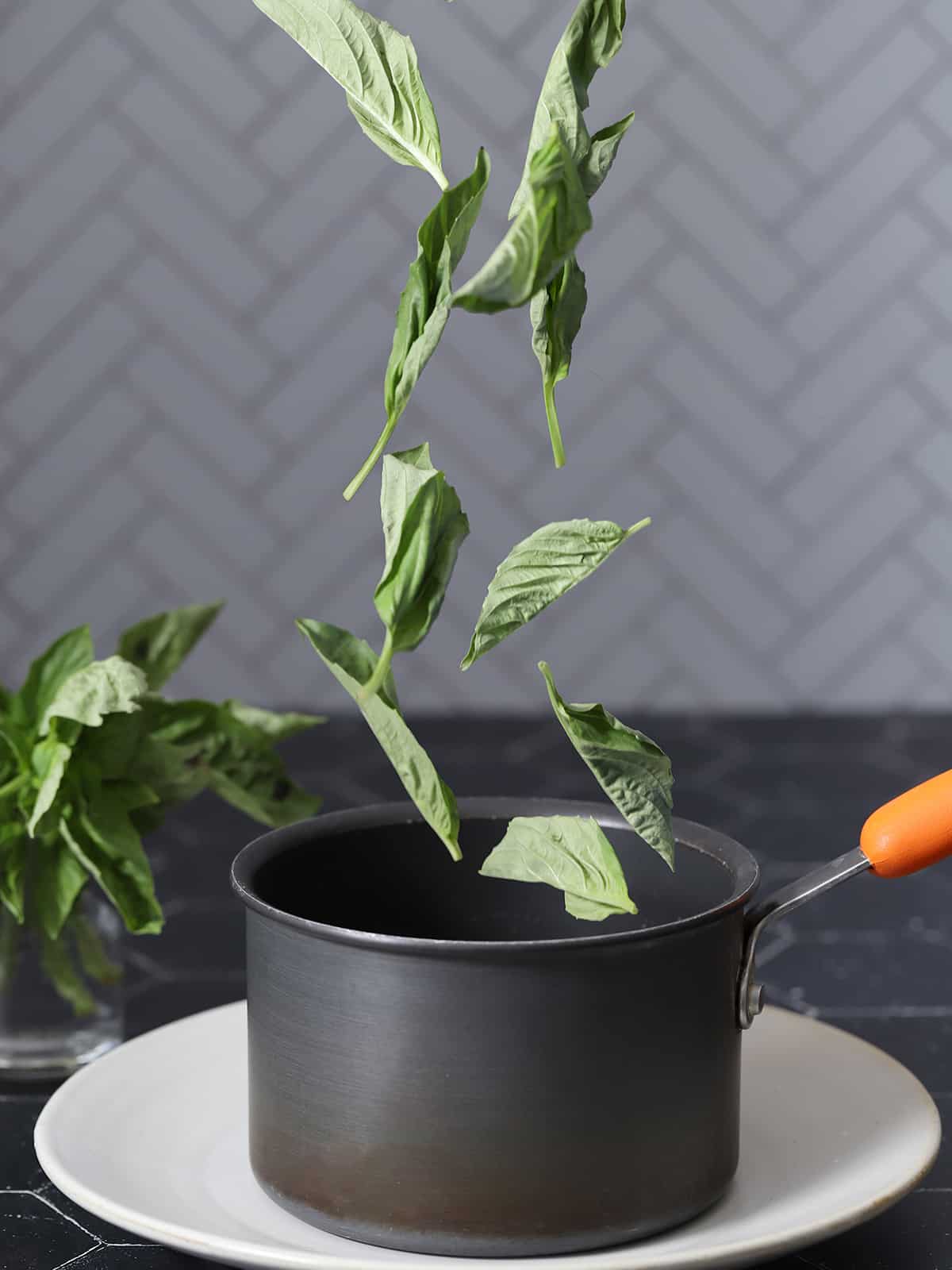 Basil leaves being dropped into a pot. 