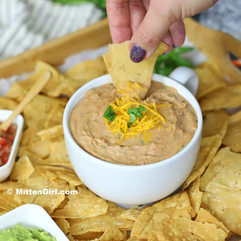 A hand scooping a chip into creamy bean dip. 