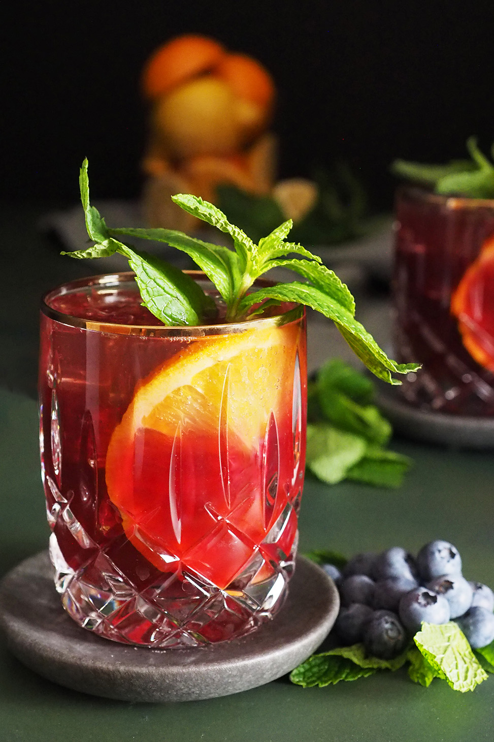 A glass filled with blueberry citrus julep garnished with a large sprig of mint and a large slice of orange.