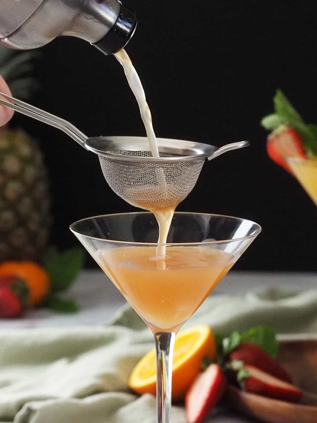 A strawberry pineapple martini being double strained into a glass. 