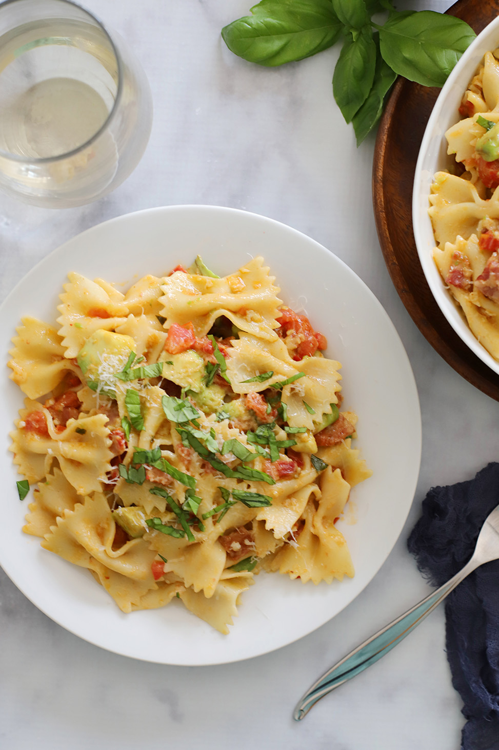 A bowl of Bacon Avocado Pasta with a fork and wine glass sitting nearby.