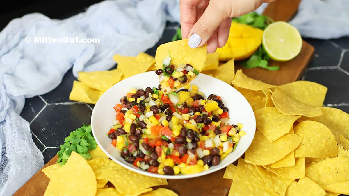 A hand holding a chip and scooping up some black bean mango salsa. 