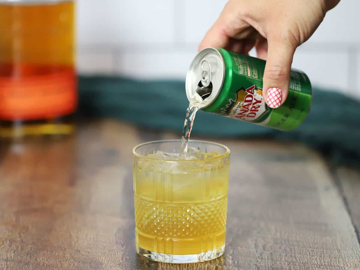 Pouring ginger ale on the top of the bourbon cocktail.