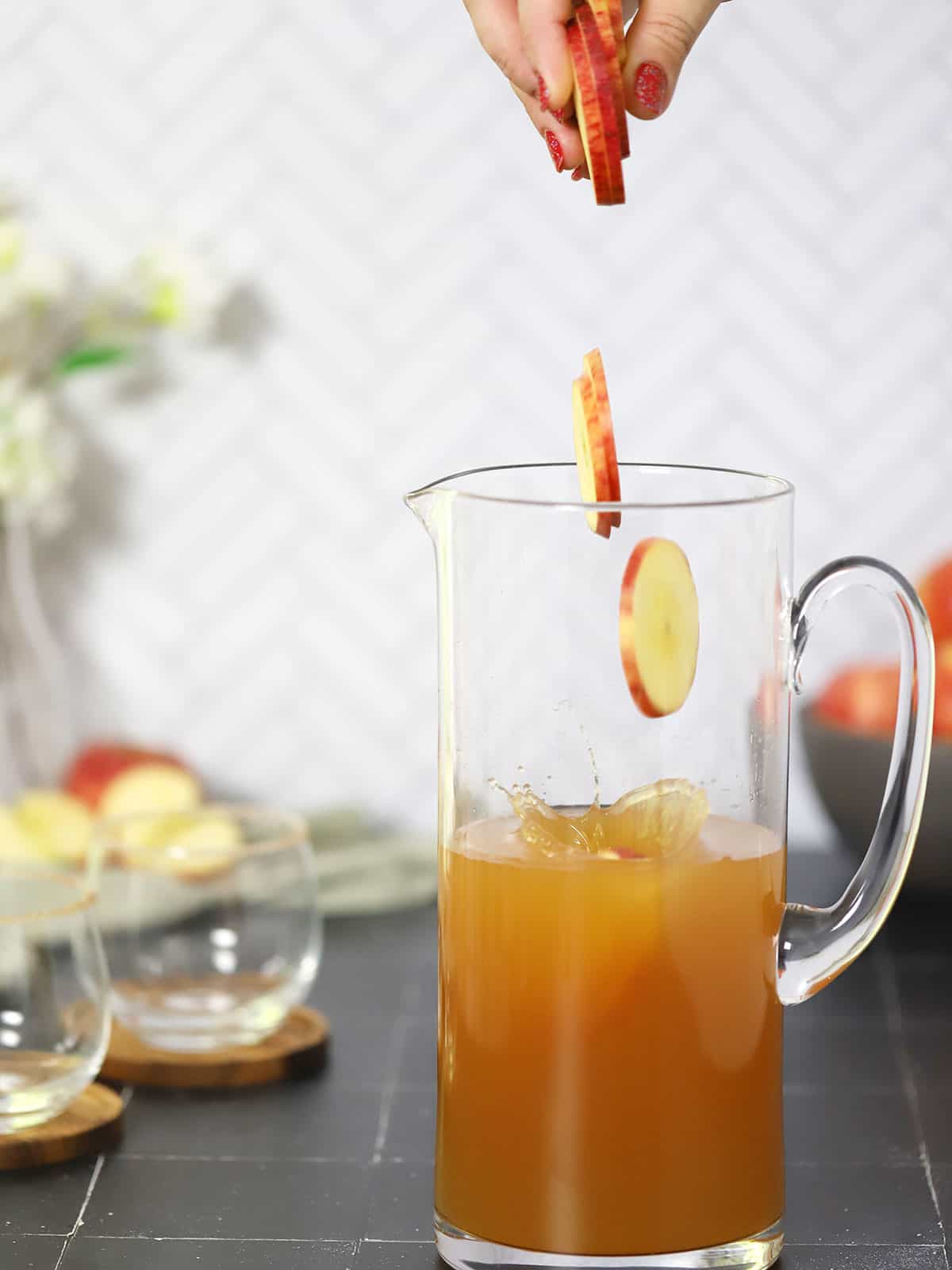 A pitcher of apple cider sangria with apple slices being dropped in it.