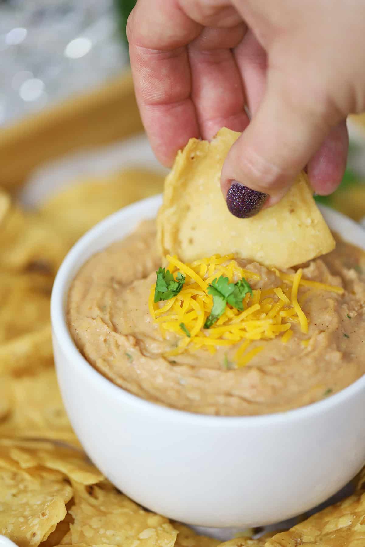 A hand with a chip scooping up some bean dip. 