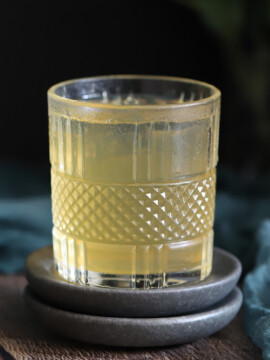 A glass of bourbon ginger cocktail on grey coasters.