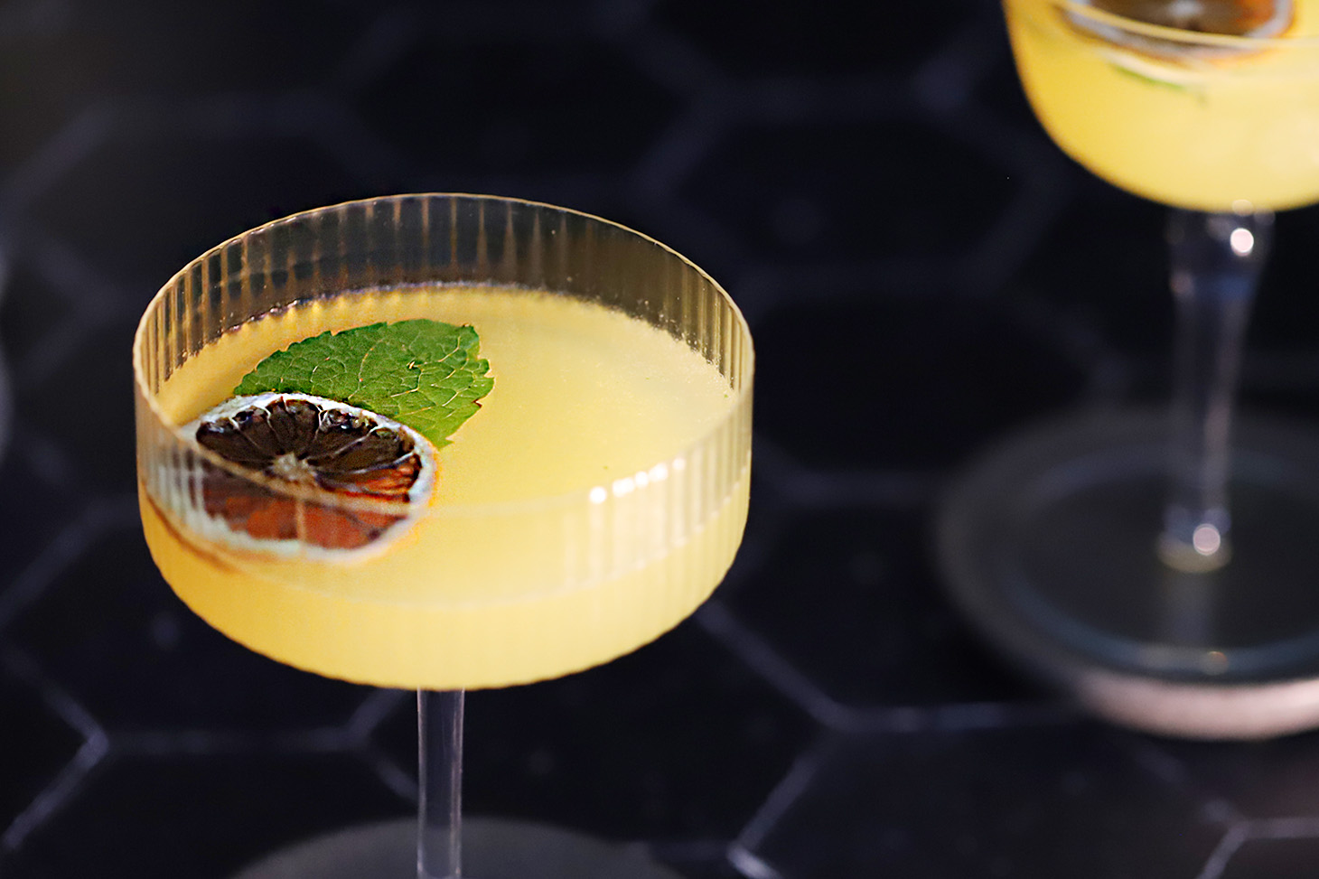 Glasses of honey orange gin cocktail garnished with dehydrated orange slices and mint leaves.