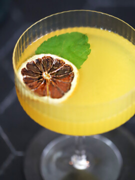 A glass of honey orange gin cocktail garnished with a dehydrated orange wheel and mint leaf.
