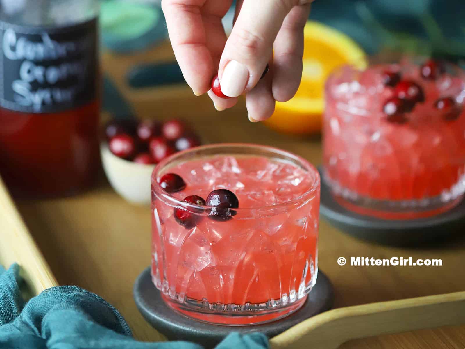 A hand adding cranberries to a Cranberry Orange Mocktail.