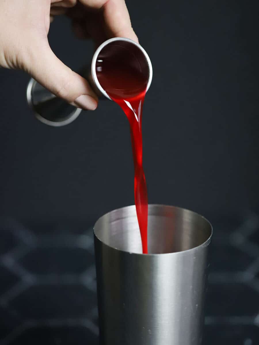 Cranberry orange syrup being poured into a cocktail shaker