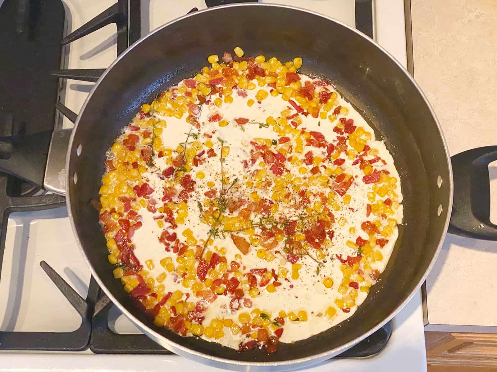 Cream in a pan with bacon, corn and thyme