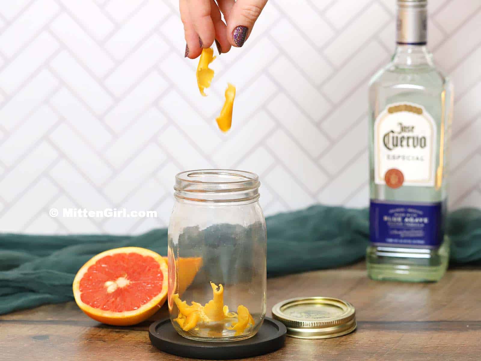 Grapefruit peel falling into an empty pint jar.