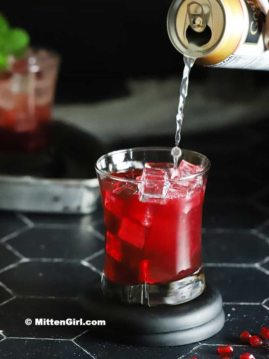 A pomegranate mocktail being topped with ginger beer.