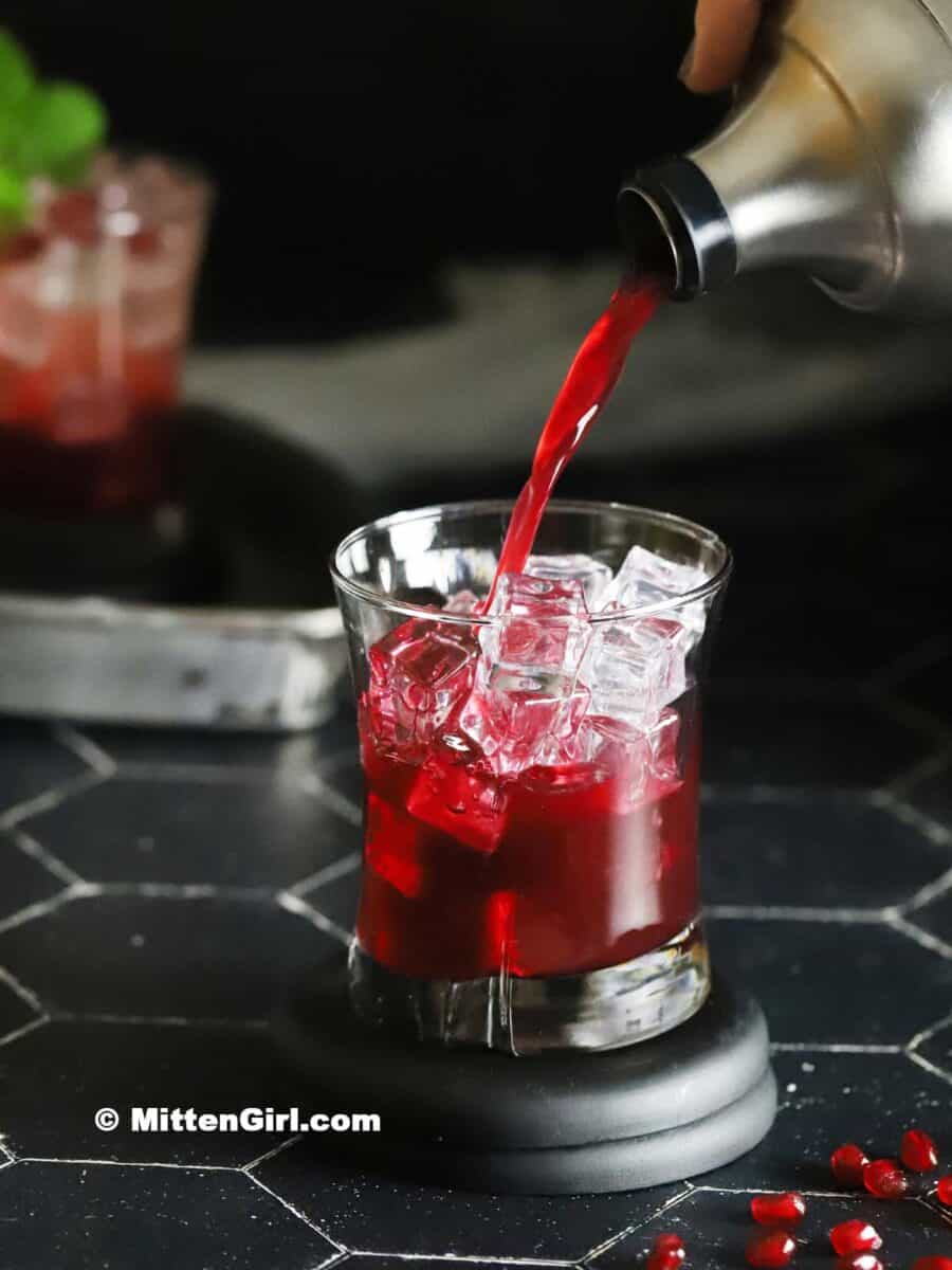 Pomegranate mocktail mix being poured into a glass filled with ice.