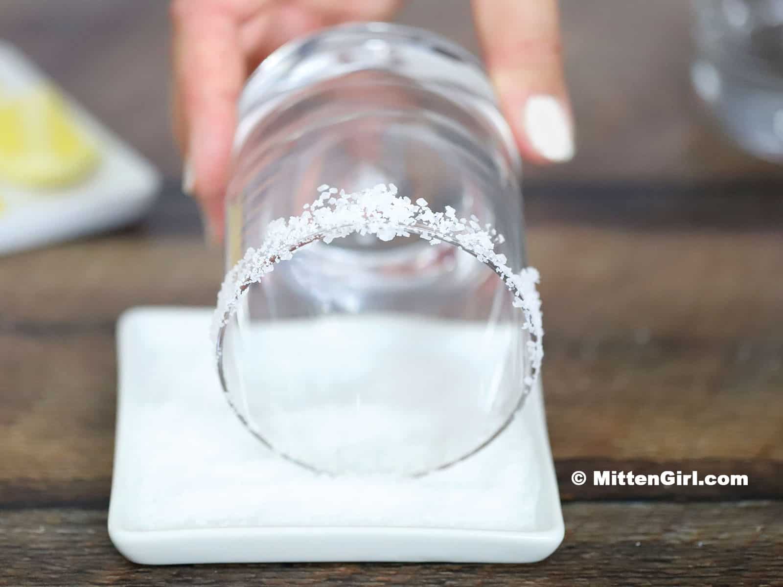The rim of a glass being dipped in a shallow dish of salt.