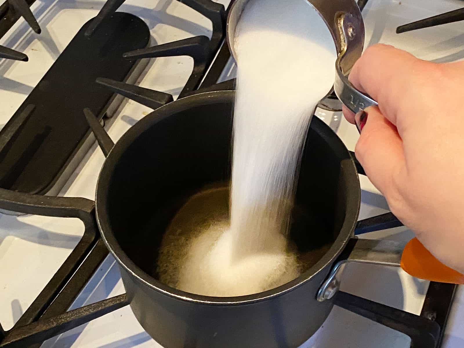 Sugar being poured into a small pot of hot water