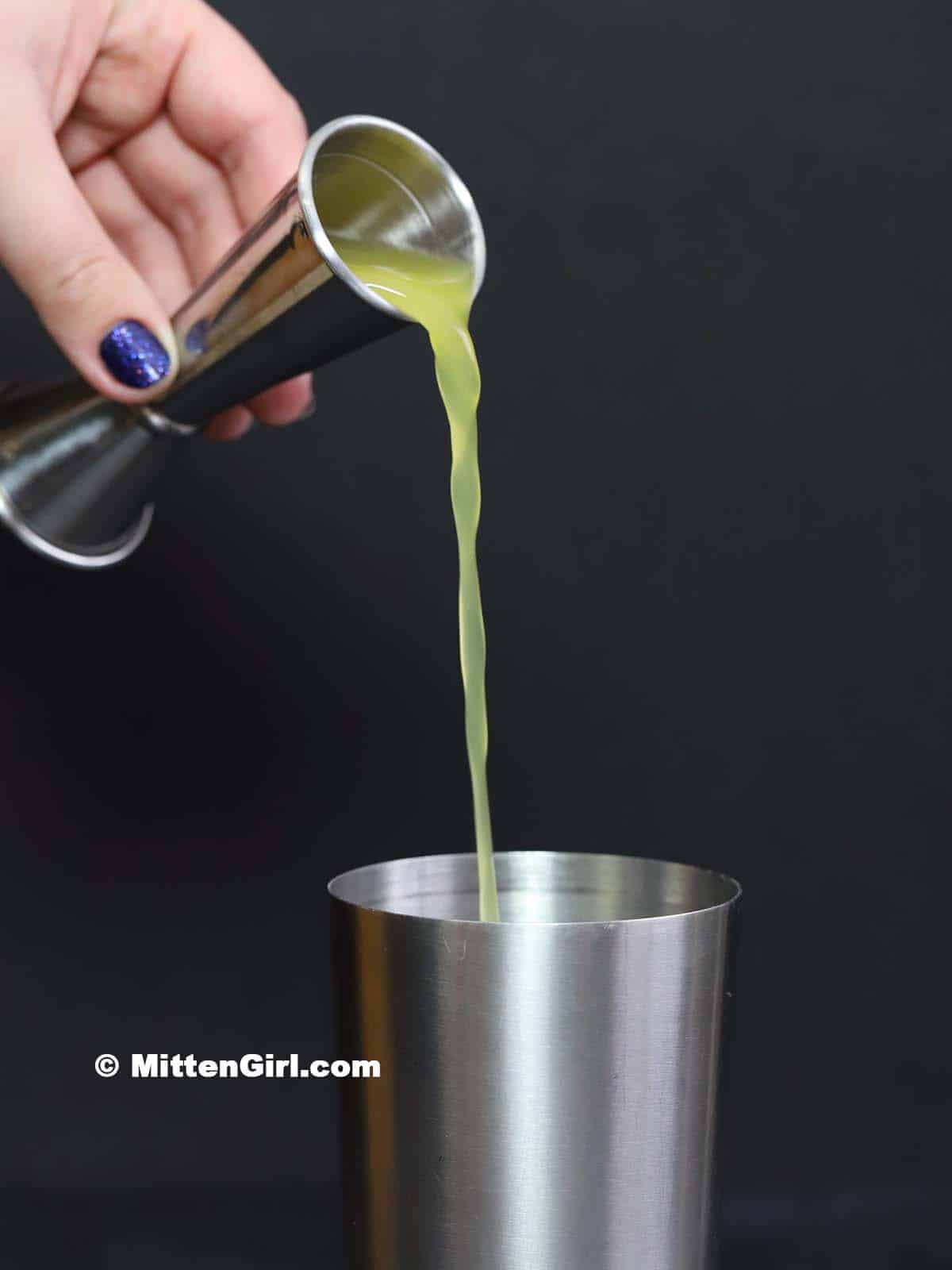 Pineapple juice being poured into a cocktail shaker