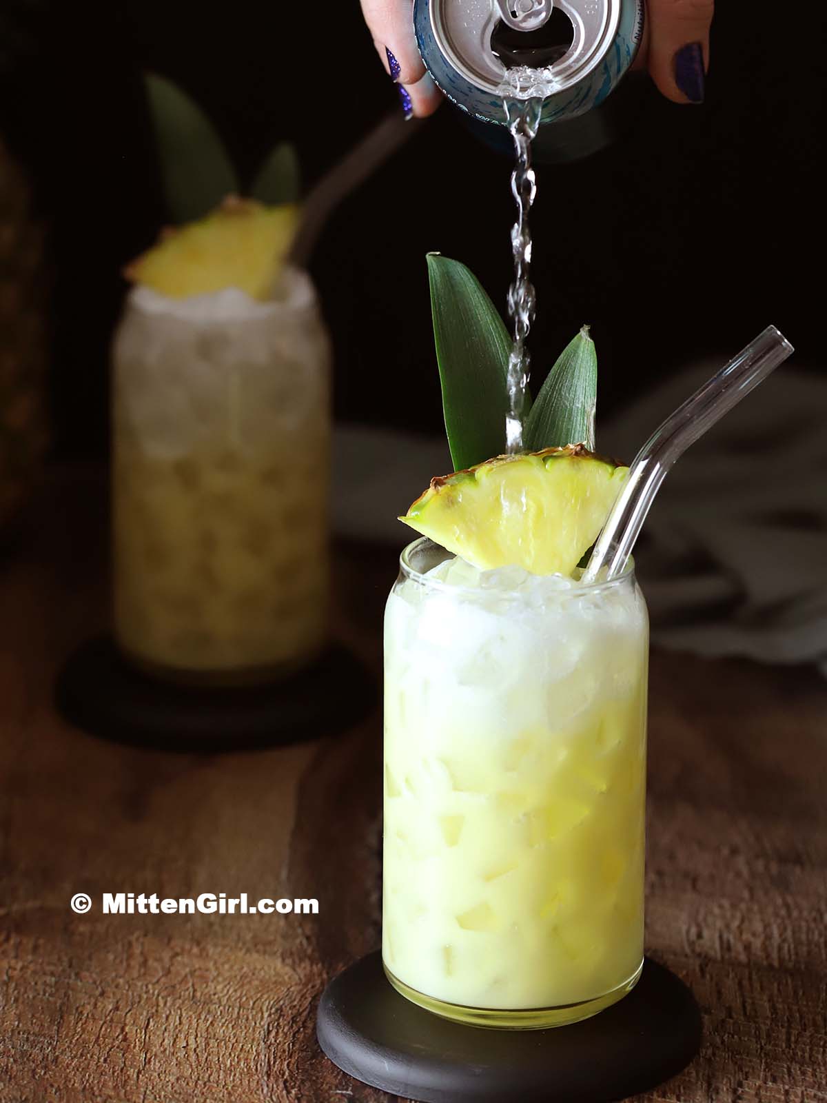 Club soda being poured on top of a pina colada mocktail. 