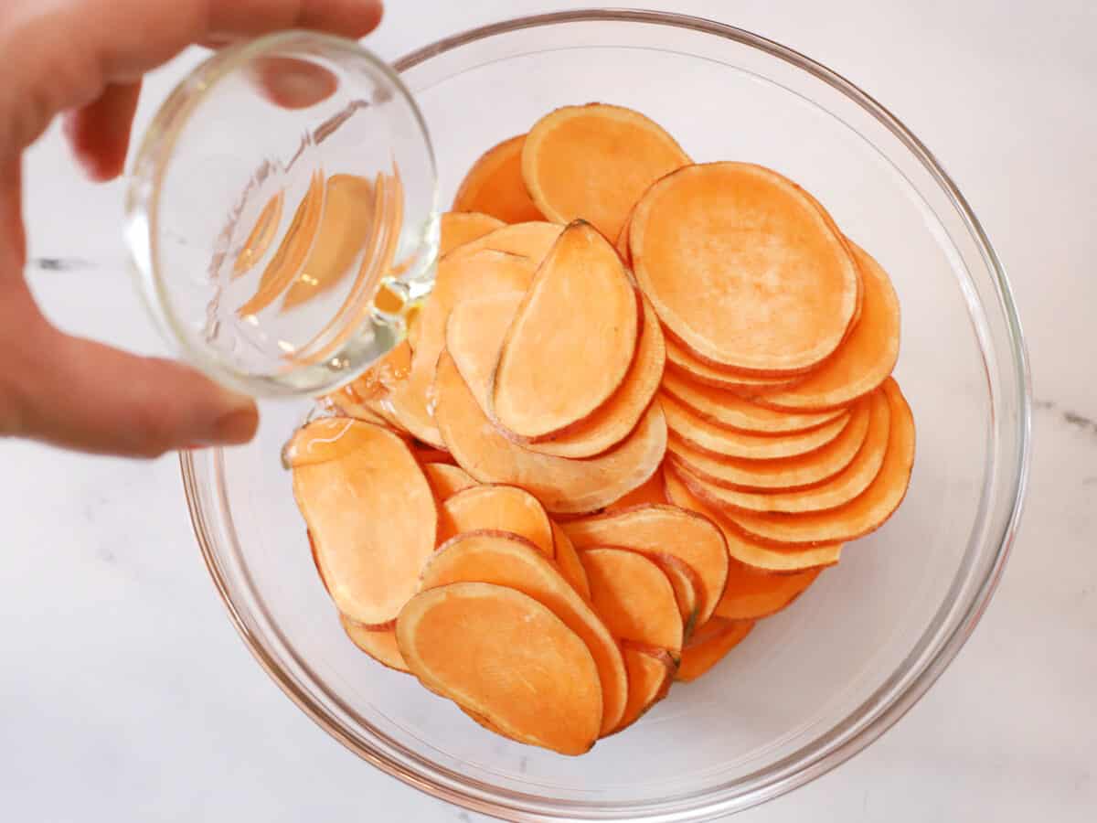 Vegetable oil being poured onto sliced sweet potatoes