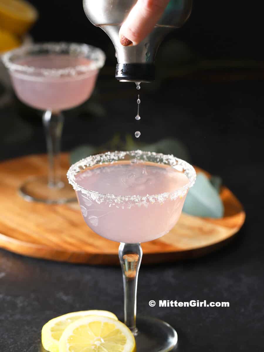 A lavender lemon drop martini being poured into a sugar-rimmed glass. 