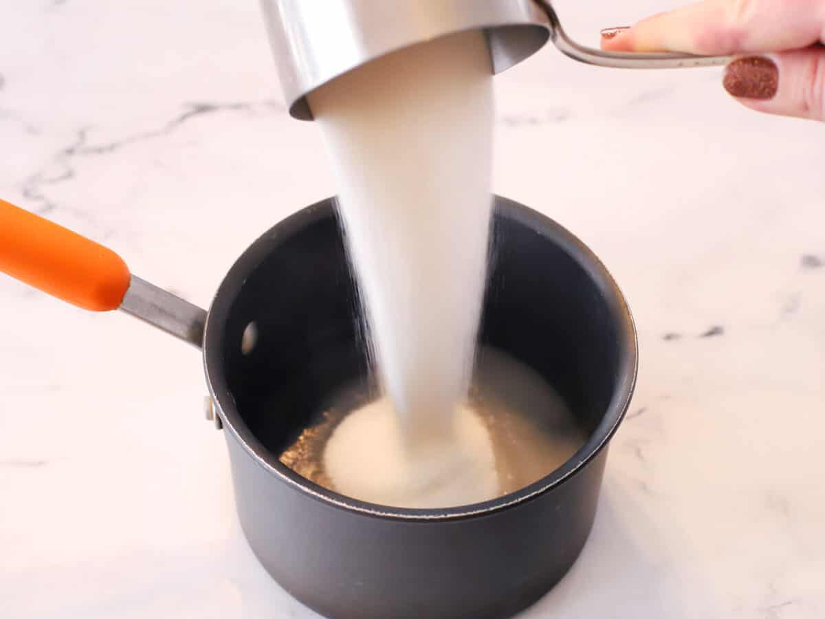 Sugar being poured into hot water in a small pot. 