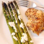 Roasted asparagus on a plate with cooked chicken.