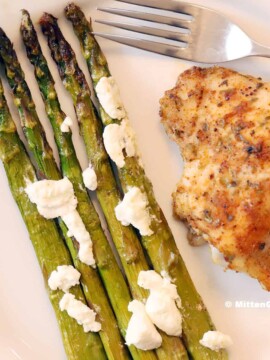 Roasted asparagus on a plate with cooked chicken.