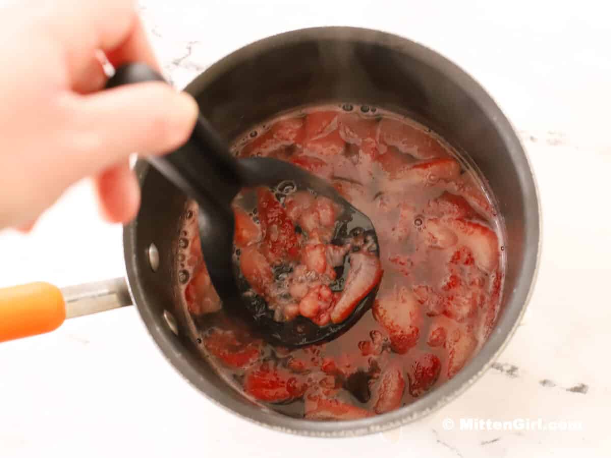 Crushing cooked strawberries in a small pot. 