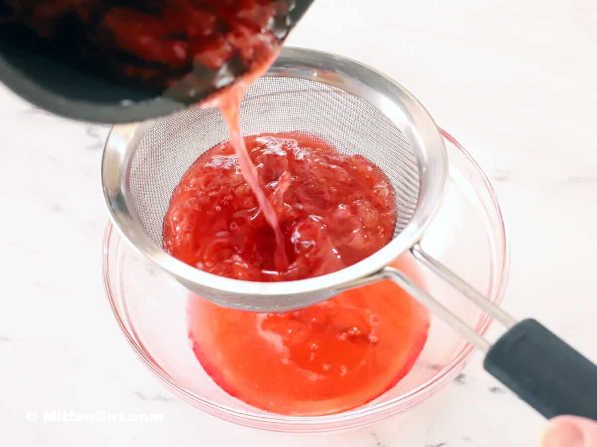 Strawberry syrup being poured through a strainer. 